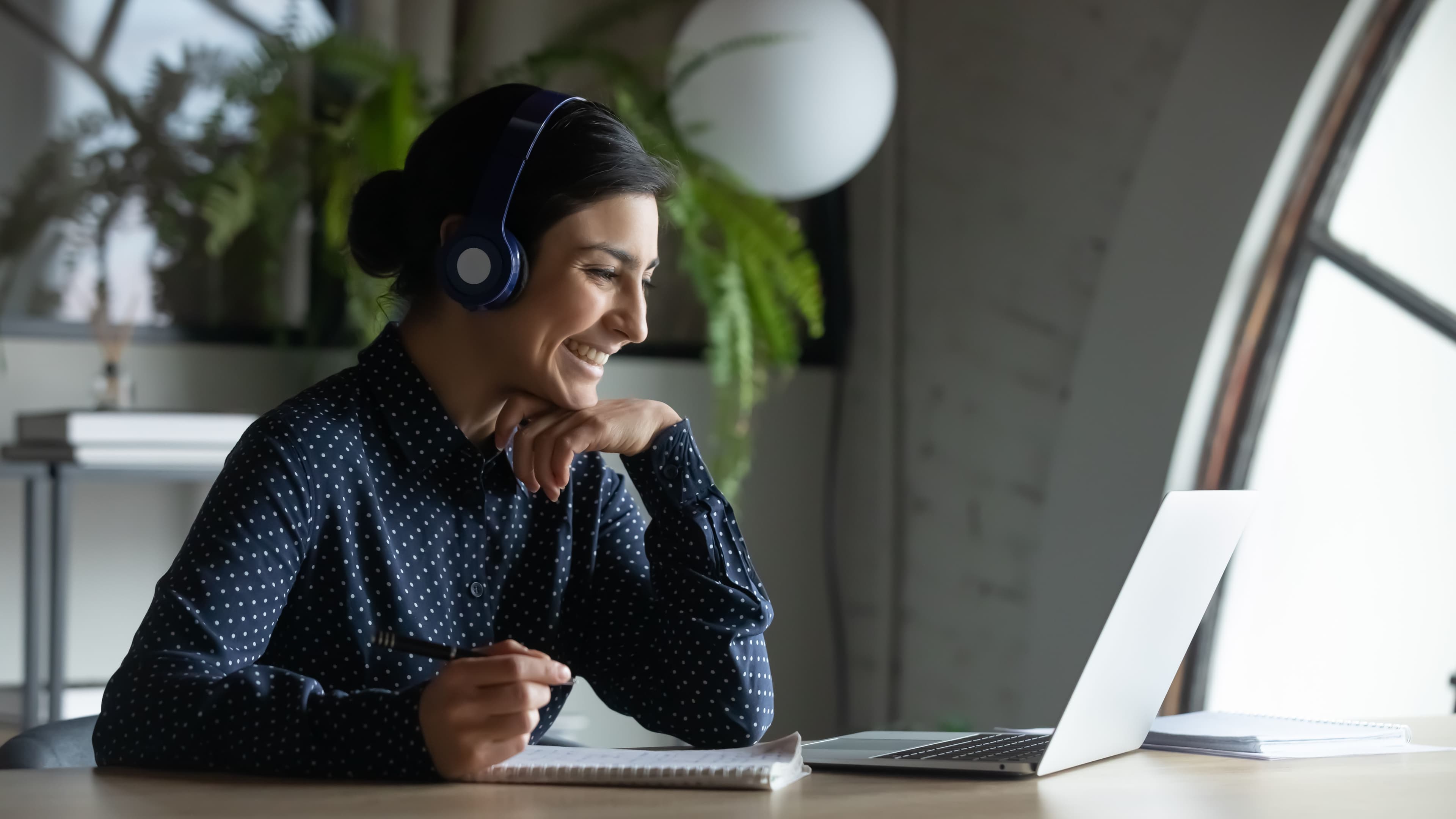 En kvinne i mørke blå skjorte med hvite prikker. Hun har på seg hodetelefoner og ser på en pc-skjerm.